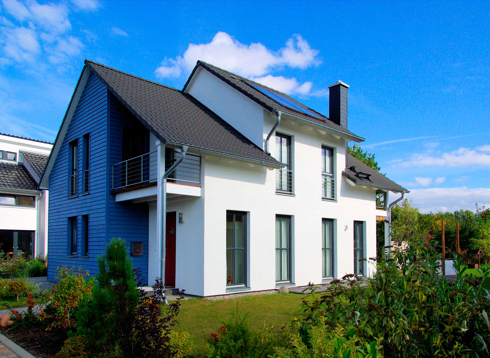 Weißes Wohnhaus mit blauer Holzverkleidung an linkem Hausteil und grauem Dach mit Garten davor